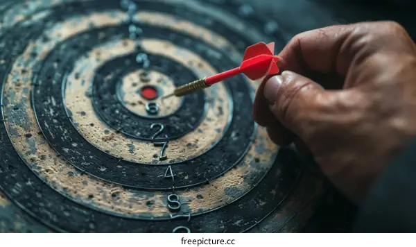 Hand holding a dart and aiming at the center of a dartboard