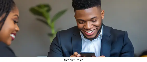 Smiling Black Man Uses Phone While Sitting In Office