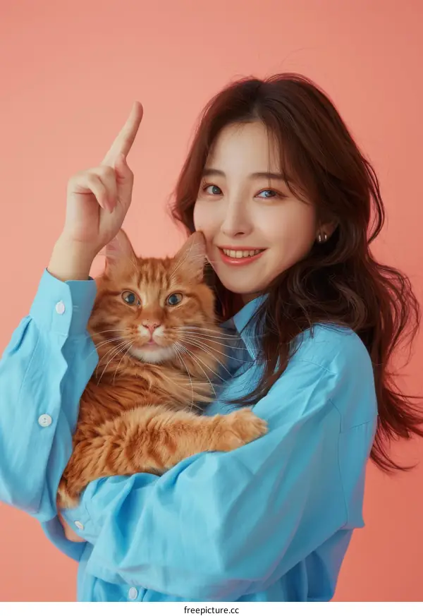 A smiling woman in a blue shirt is holding an orange cat.