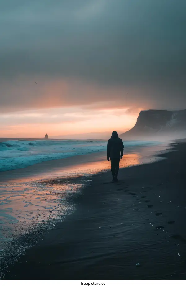 Man walking alone on a black sand beach at sunset