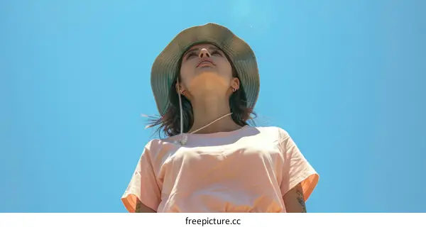 A young woman wearing a hat is looking up at the sky