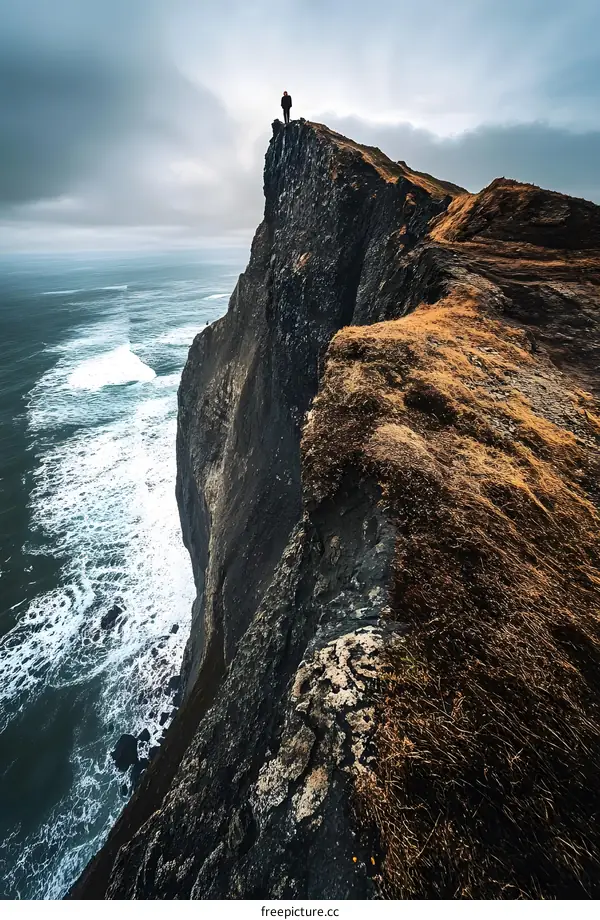Solitary Figure Standing on Cliff Edge overlooking Ocean