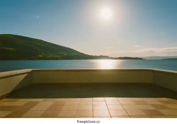 Sunlit Terrace Overlooking Calm Blue Lake with Green Hills