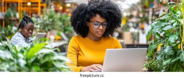 African American Woman Working on Laptop in a Greenhouse