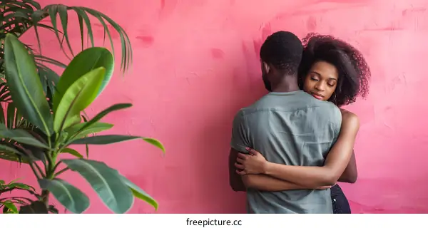 A man and a woman are hugging each other in front of a pink wall.