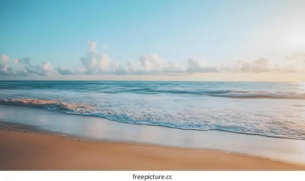 Calm Ocean Waves Crashing on Sandy Beach with Blue Sky and Clouds
