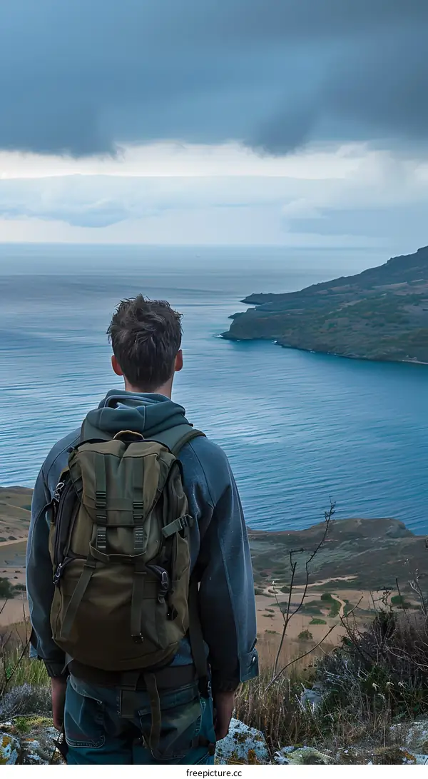 Man With Backpack Stands Looking Out at the Ocean
