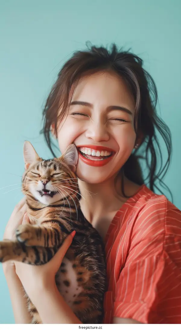 A young woman is laughing while holding a cat