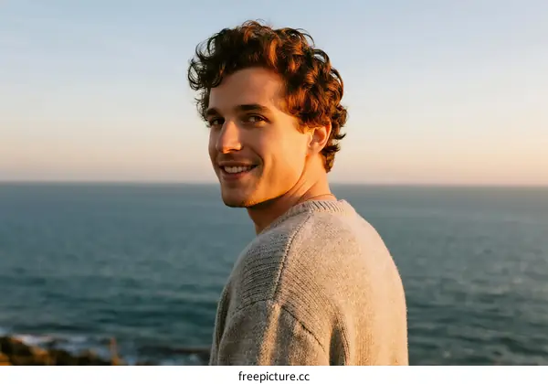 A man with curly hair standing by the seaside enjoying the view