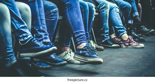 People Wearing Jeans and Sneakers Sitting in a Row