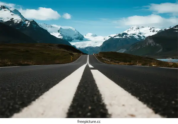 A scenic road leading towards snow-capped mountains under a clear blue sky