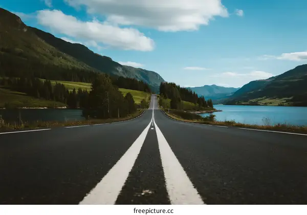 A scenic road leading through mountains and near a lake under a clear sky