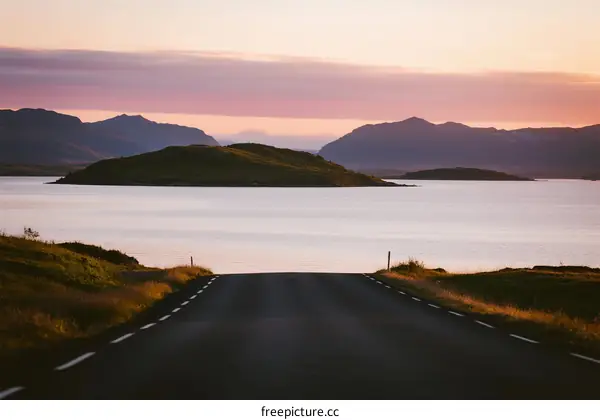 A scenic road leading to a tranquil lake with mountains in the distance