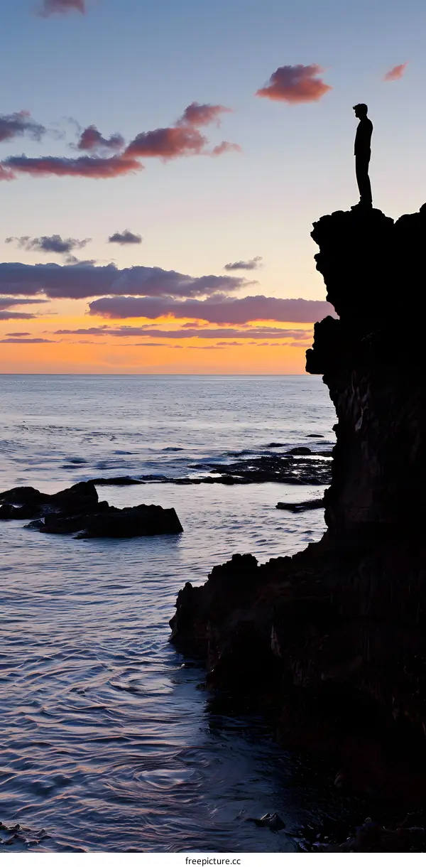 Silhouette of Man Standing on a Cliff Overlooking the Sea at Sunset
