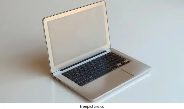A silver macbook laptop sits on a white table.