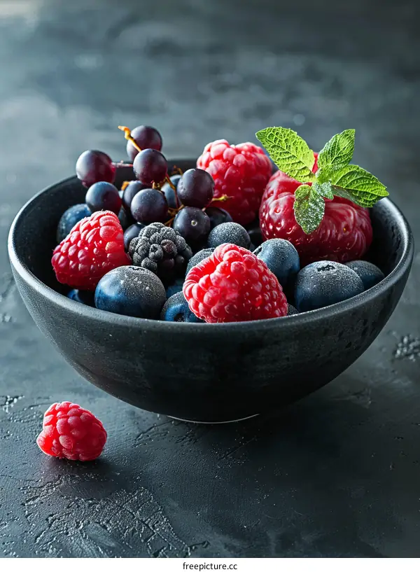 Black bowl with fresh blueberries, raspberries and blackberries on a dark background