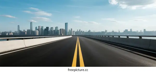 A clear road leading to a modern city skyline under a blue sky