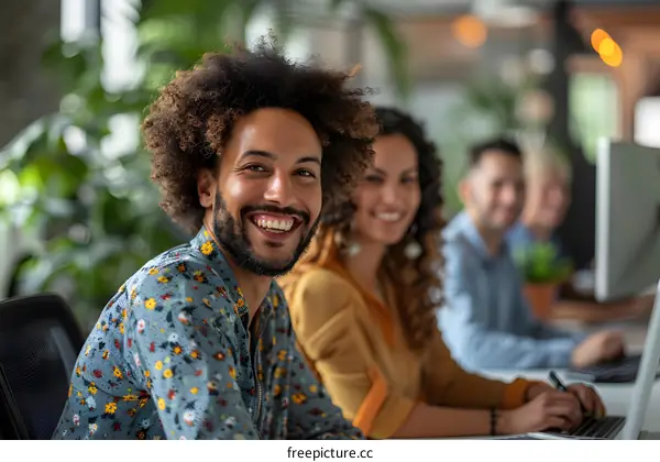 Portrait of a smiling man with afro hair in a casual shirt surrounded by his colleagues in the background