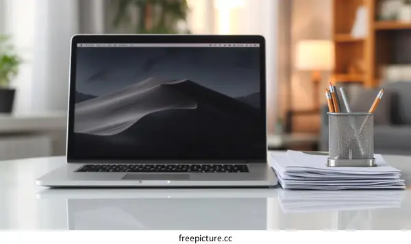 A desk with a laptop, a pencil holder, and a stack of paper