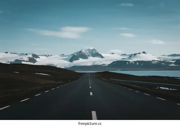 Long road leading to snowy mountain range under clear sky