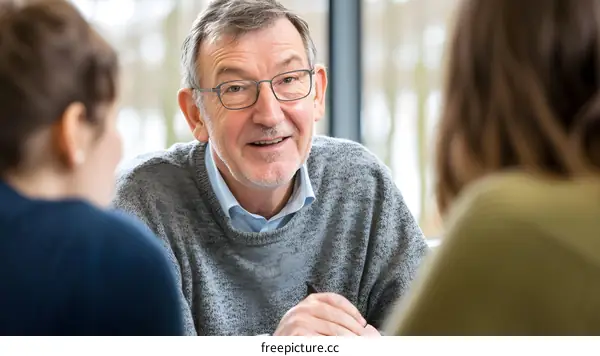 Senior Man Speaking to Two Younger Women in Meeting