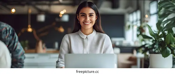 Smiling Hispanic Woman Using Laptop In Modern Office