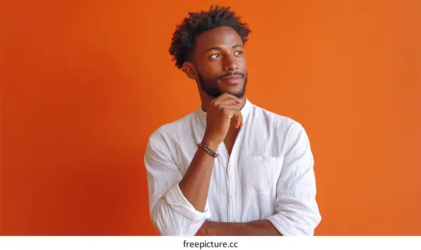Young African man in white shirt thinking against orange background