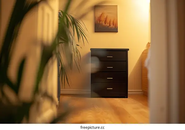 Black four drawer dresser with a plant and painting in the background