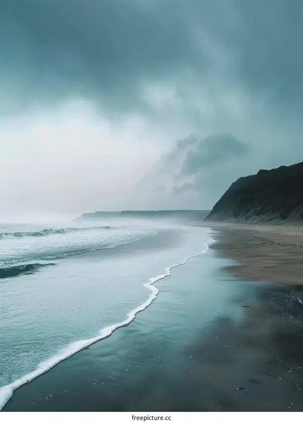 The dark foggy sea is hitting the beach with small waves