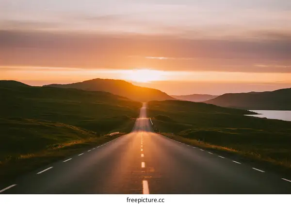 Sunset over a long empty road with rolling hills in the distance