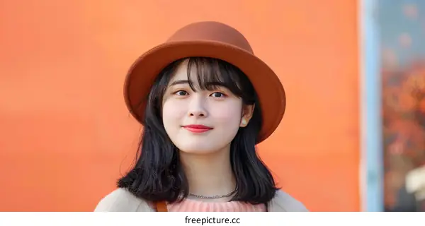 Young Woman Wearing a Brown Hat Against a Orange Wall