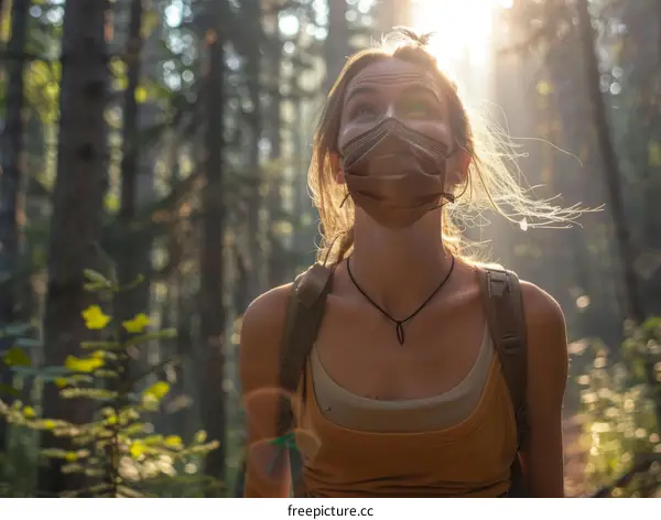 Young woman wearing a mask in the woods looking up at the sun