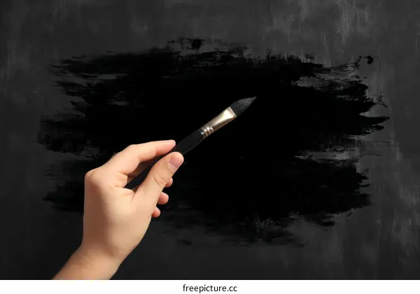 Hand holding paintbrush on dark background with artistic splash