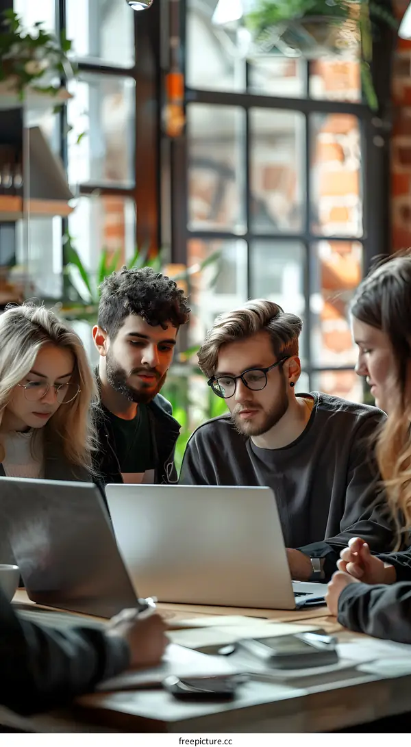 Four young people sitting at a table and looking at a laptop