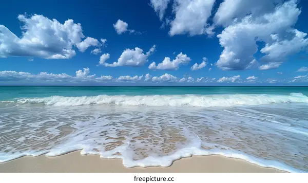 gentle waves rolling onto a sandy beach under a blue sky with white clouds