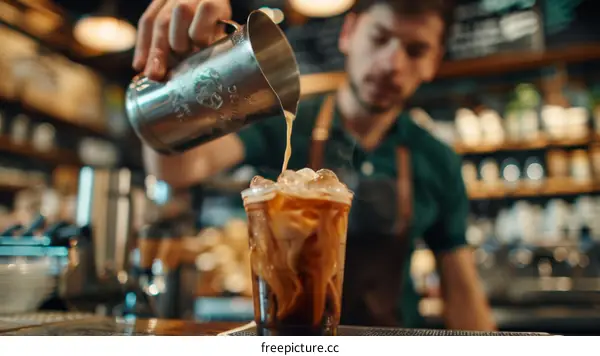 Barista pouring milk into iced coffee