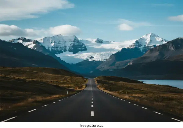 Long road leading to snow-capped mountains under a clear sky