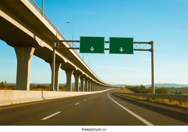 A long highway with an overpass and green road signs indicating directions