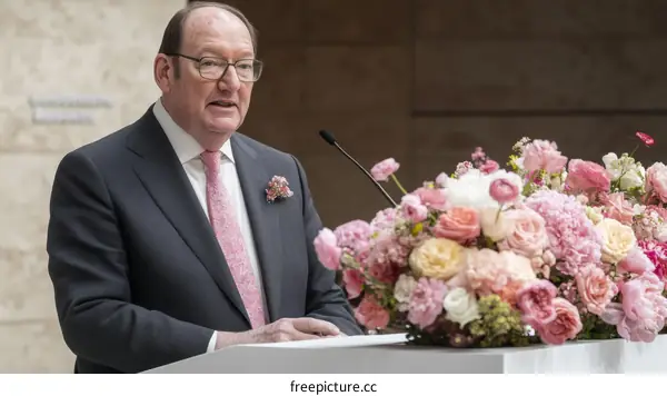 Man in suit giving a speech surrounded by flowers