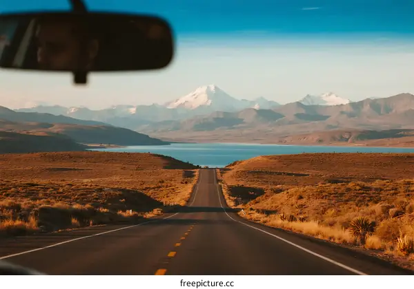 Scenic Road Leading to Snow-Capped Mountain and Calm Lake