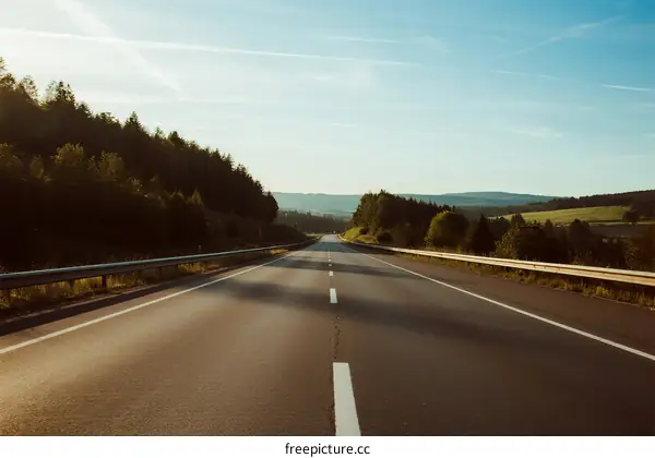 A peaceful highway with clear sky and lush green trees on both sides