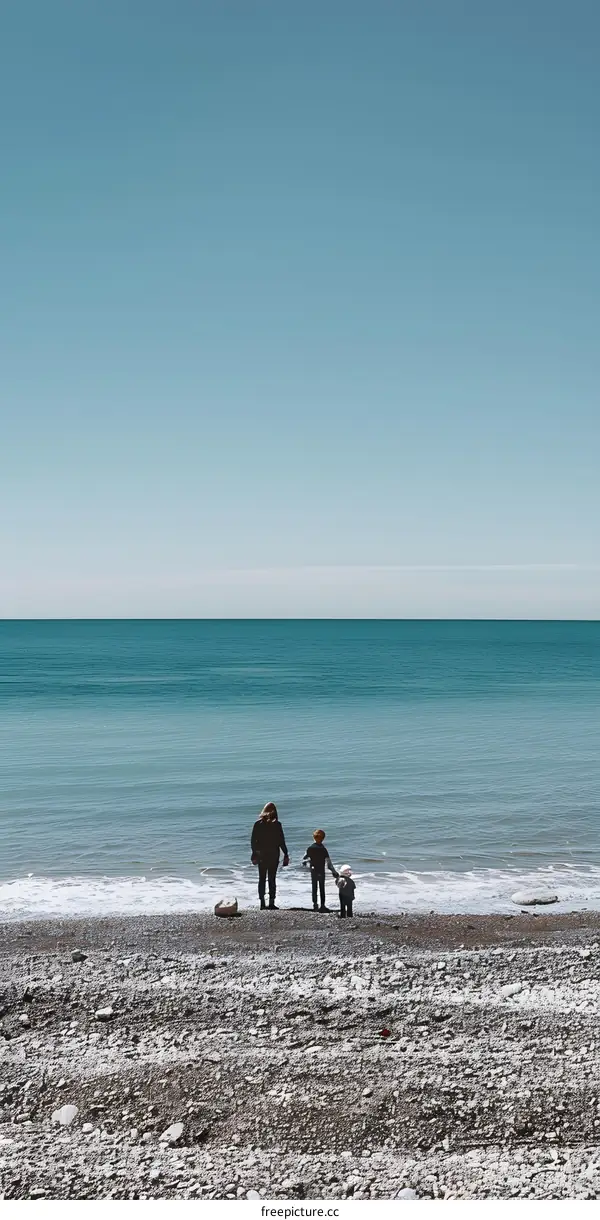 Family of Three Standing on a Pebble Beach Facing the Ocean