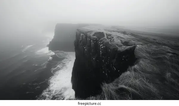black and white photo of a cliff edge overlooking a foggy ocean