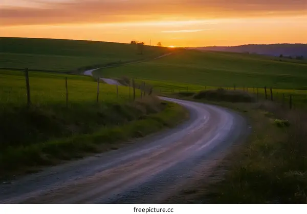 Sunset over a winding country road through green fields