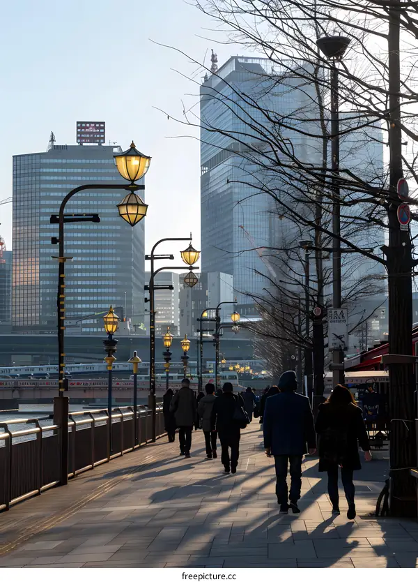 People Walking Along River Path with Streetlights and City Buildings in Background