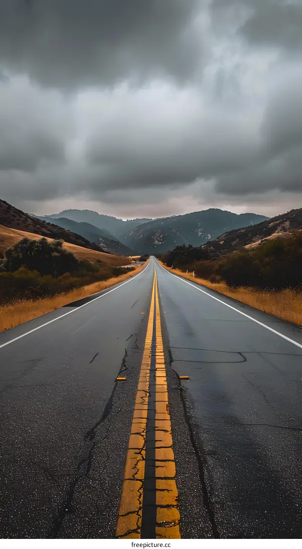 Empty Road Leading to Mountains Under Stormy Sky