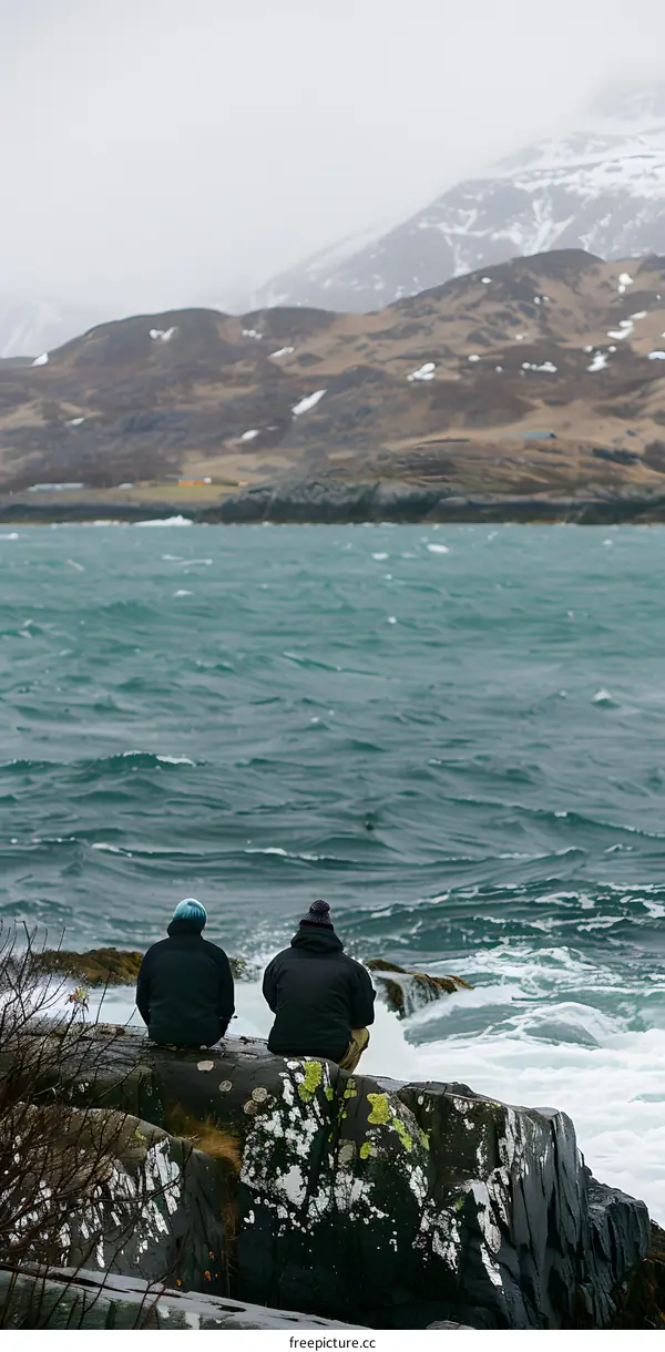 Two Men Sitting on a Rocky Cliff Overlooking the Ocean