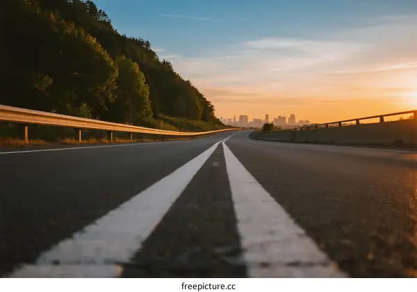 A scenic road with white lines leading to a city at sunset