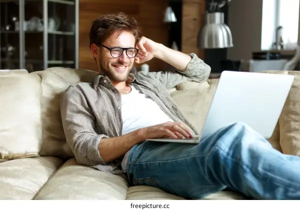 Smiling Man Relaxing on Sofa with Laptop