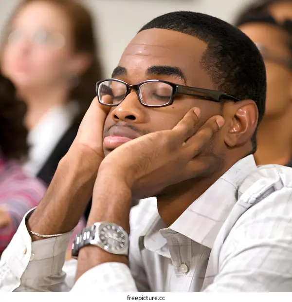 Black Man Wearing Glasses and a Wristwatch With His Head Resting on His Hands